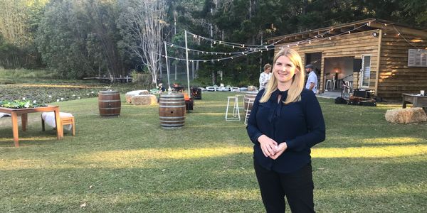Woman standing in a grassy outdoor space with a wooden cabin and barrels.