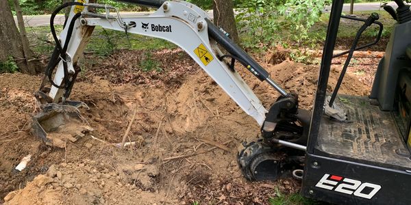 Excavator digging hole for residential septic tank installation during septic system construction.