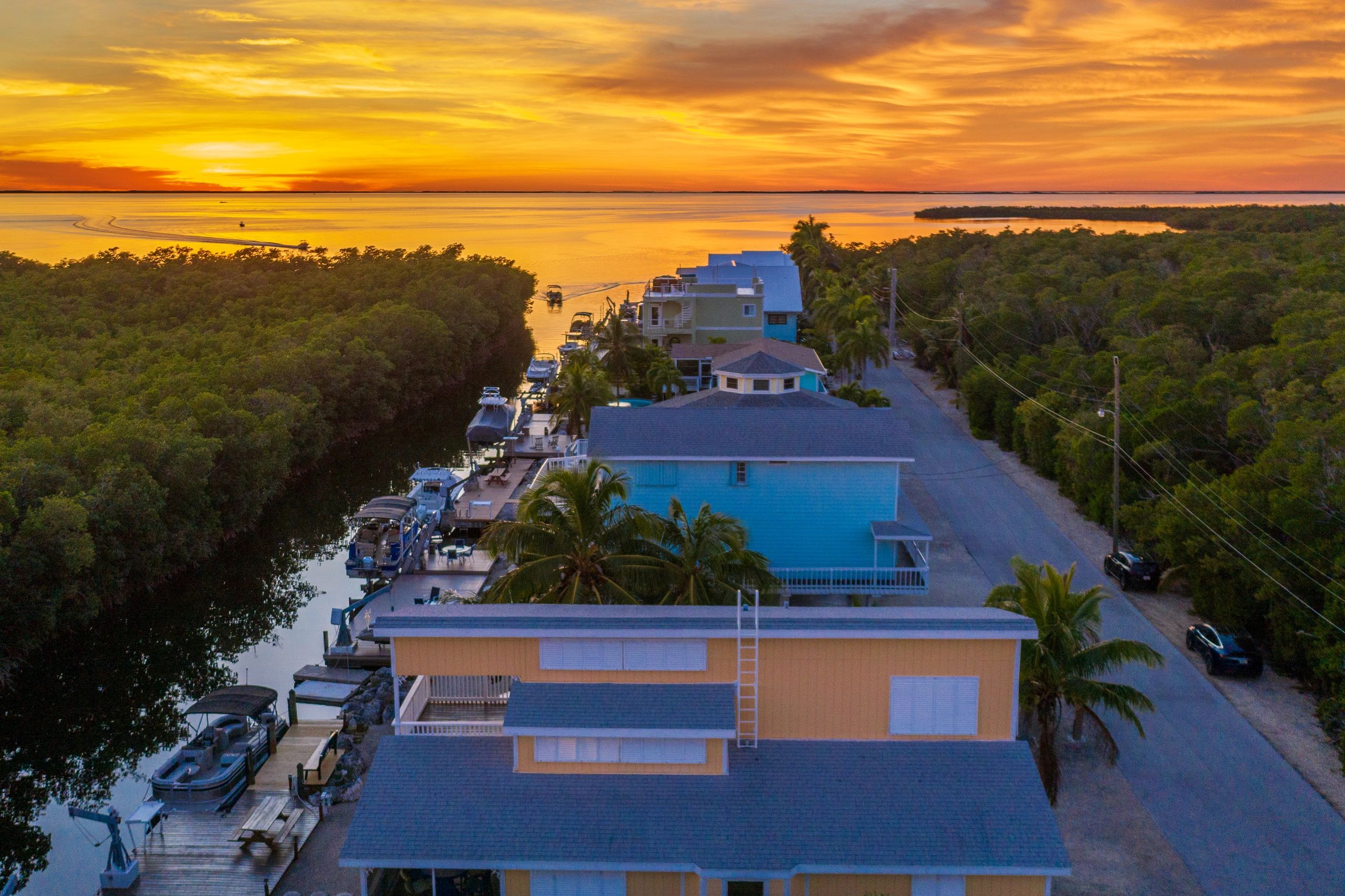 Sunset drone view of vacation rental, mangroves and canal with boats looking out to the open bay.