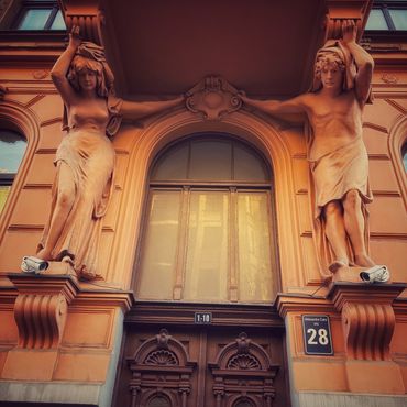 Ornate building entrance supported by classical male and female statues.