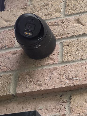 Black security camera mounted on a brick wall.