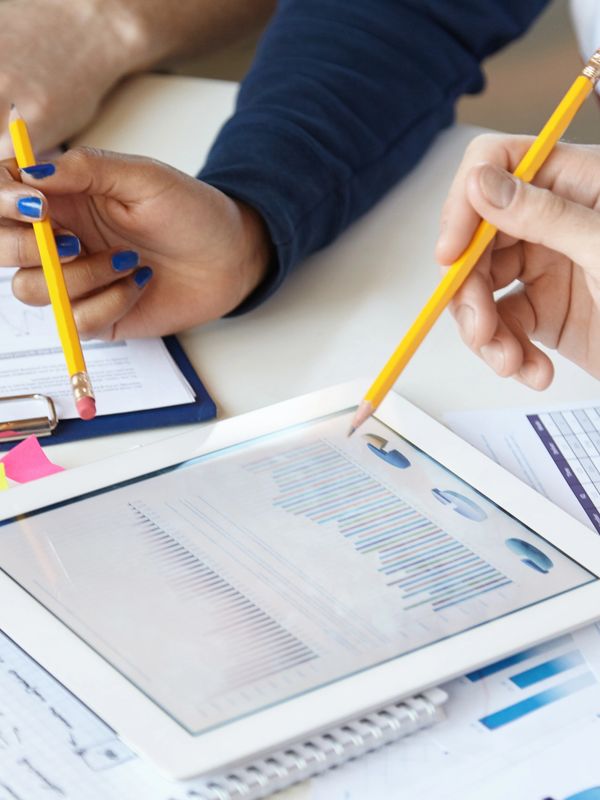An image of an iPad, notebooks and sticky notes with hands of three people holding pencils working.