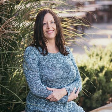 A woman in a blue sweater and jeans sitting outdoors on a stone bench.