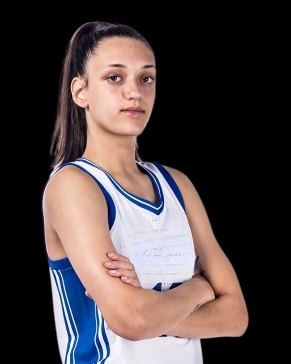 Female basketball player posing confidently in white and blue jersey.