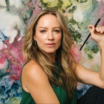 Woman artist posing with paintbrush in front of colorful abstract painting.