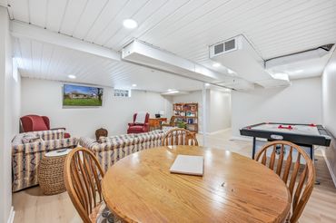 Downstairs family room with plenty of seating, a work table with power outlet and an air hockey tabl