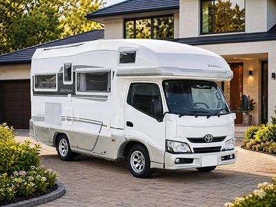 White camper van parked in front of a modern house on a sunny day.