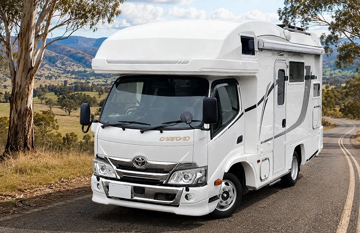 White camper van parked on a scenic road with hills in the background.