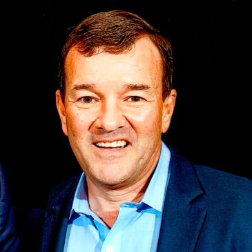 Man smiling in blue shirt and dark jacket.