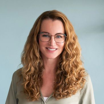 Smiling woman with curly hair and glasses.