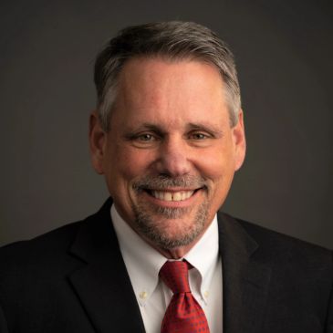 Smiling middle-aged man in a suit and red tie.