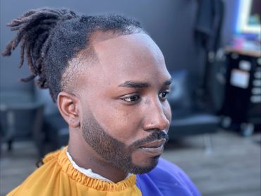Man with a fresh haircut and beard trim sitting in a barber's chair.