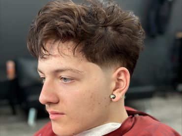 Young man with a fresh haircut wearing a red barber cape.