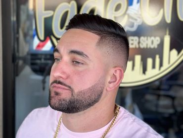 Man with fresh fade haircut and well-groomed beard posing outside a barbershop.