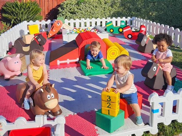 Children playing happily in a colorful outdoor playpen with soft toys and blocks.