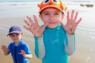 Two small boys on the beach holding up their hands to show that they are covered in sand. The larger