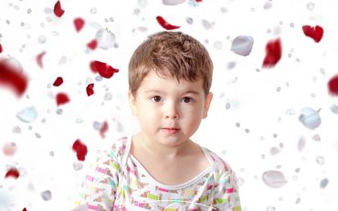 Young child surrounded by falling red and white rose petals.