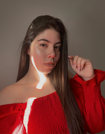 Young woman with long hair wearing a red off-shoulder top illuminated by sunlight.