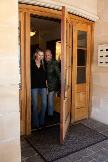 A couple exits through a wooden door into a building lobby.