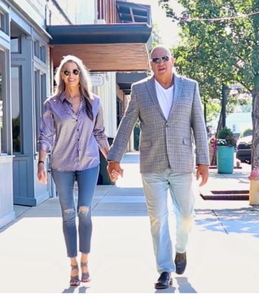 A couple holding hands and walking on a sunny sidewalk in a casual yet stylish outfit.