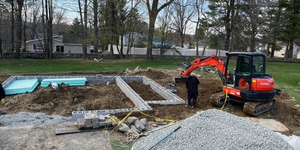 Construction site with foundation work and mini excavator in a suburban area.