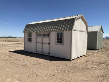 A small beige shed on a dirt lot under clear blue sky.