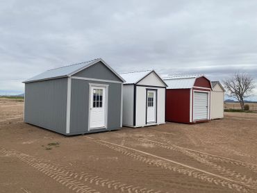 Four outdoor sheds in different colors stand on a bare dirt ground.
