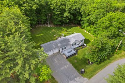 A single-story house surrounded by lush green trees and a driveway.