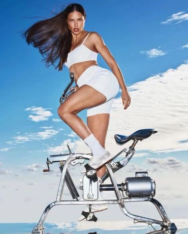 Woman in white activewear posing on exercise bike outdoors.