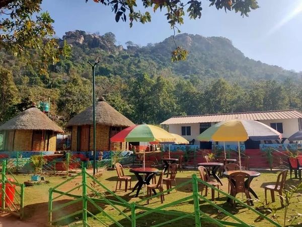 Outdoor seating area with umbrellas near traditional huts and a mountain backdrop.