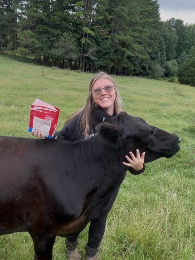 Woman smiling with black cow in green field.