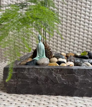 Miniature Buddha statue with stones and green plant in a textured pot.