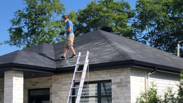 Man wearing mask and gloves sprays roof on a sunny day.