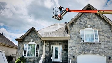 Worker uses lift to pressure wash a house roof on a cloudy day.