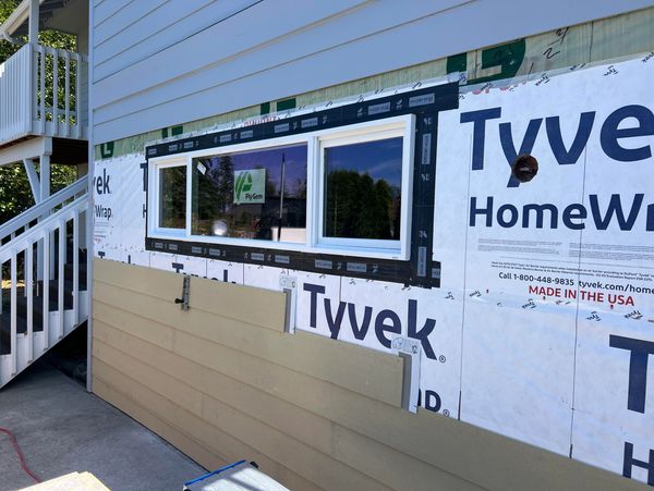 Window installation in progress on house with Tyvek HomeWrap and beige siding.