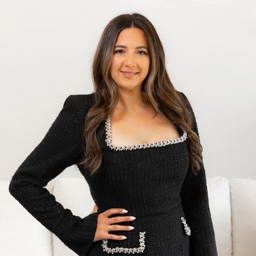 Woman in a stylish black dress with pearl details, smiling confidently.