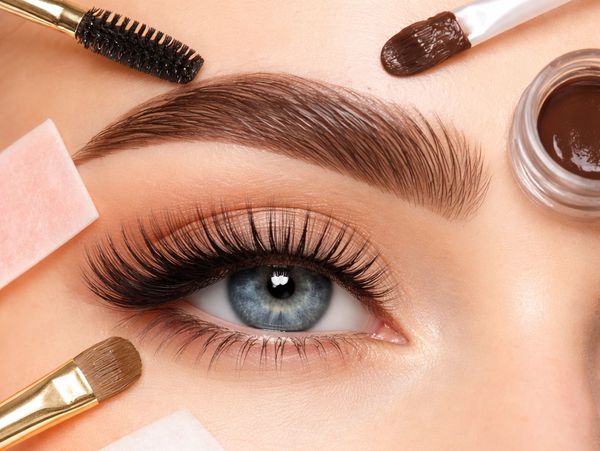 Close-up of a blue eye with long lashes and eyebrow makeup tools.