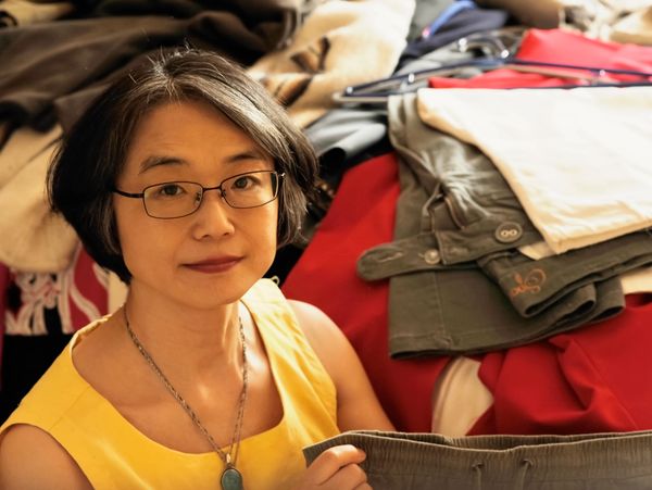 Woman in glasses holding clothes, surrounded by folded garments.