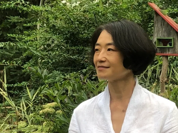 Woman in white shirt standing in a lush garden looking to the side.