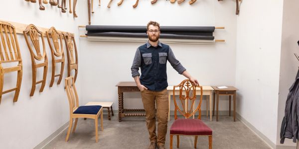 Man standing in a workshop with wooden chairs.
