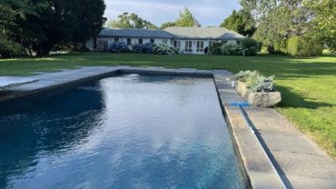 Modern backyard with a rectangular pool and a white house in the background.