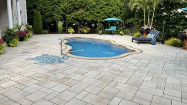 Backyard pool area with stone patio and lounge chairs under trees.