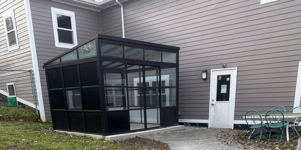 A small black greenhouse attached to a house.