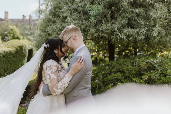 A bride wearing a white wedding dress and veil stands with her hands on her groom's shoulders.