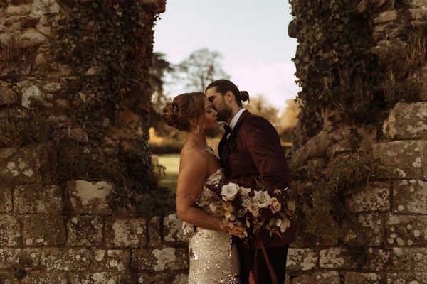 A bride and groom stand in front of an archway in Jervaulx Abbey in Yorkshire.