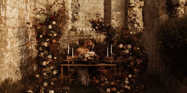 A bride and groom sit at a sweetheart table surrounded by flowers and candles.