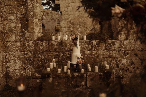 A white wedding cake, dressed with flowers and surrounded by candles at Jervaulx Abbey in Yorkshire.
