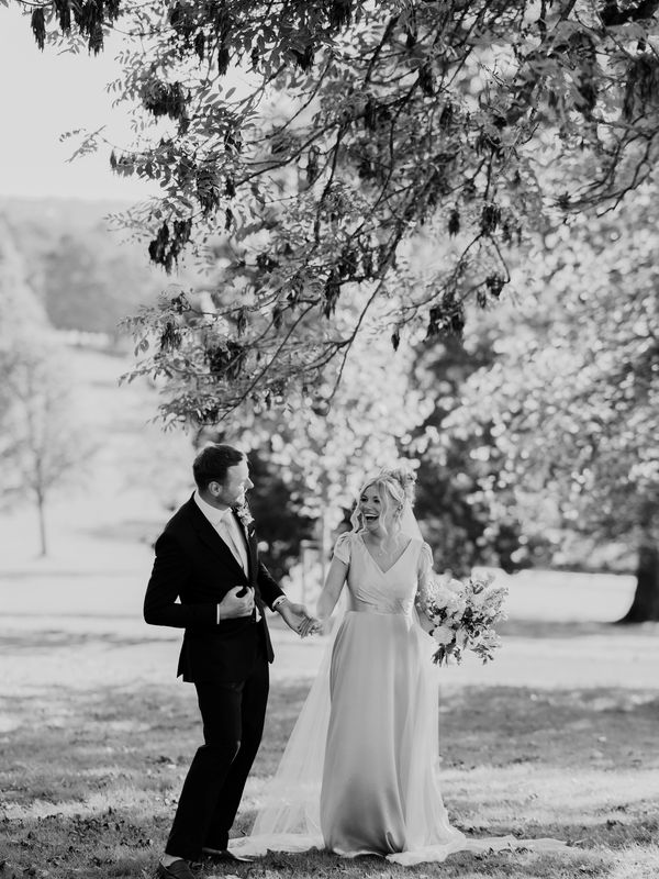A bride and groom laugh as they walk through the park at The Mansion in Leeds, Yorkshire.