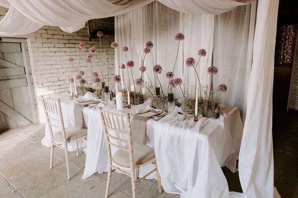 A table dressed with a white tablecloth and purple flowers, candle sticks and place settings.