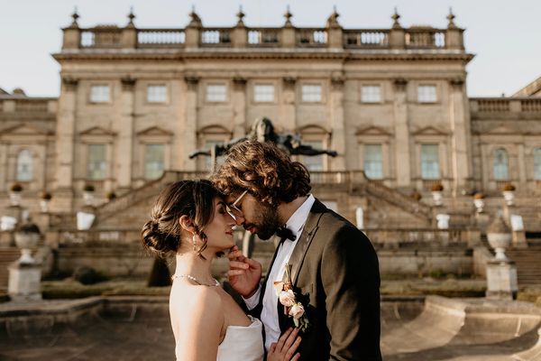 A woman and a man stand with their foreheads touching in front of Harewood House in Yorkshire.